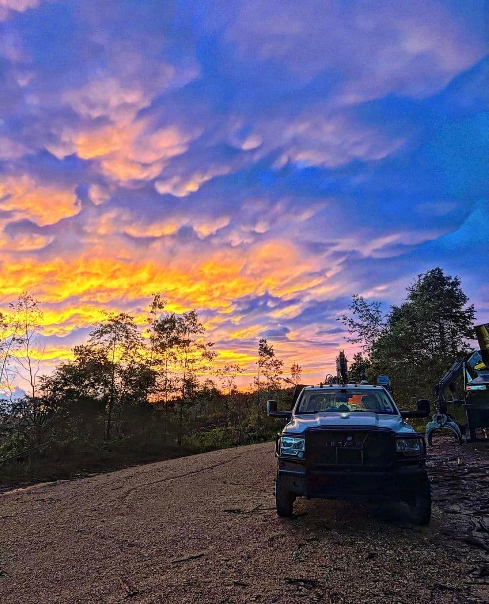 Truck parked on a scenic rural road during a vibrant sunset with colorful clouds.