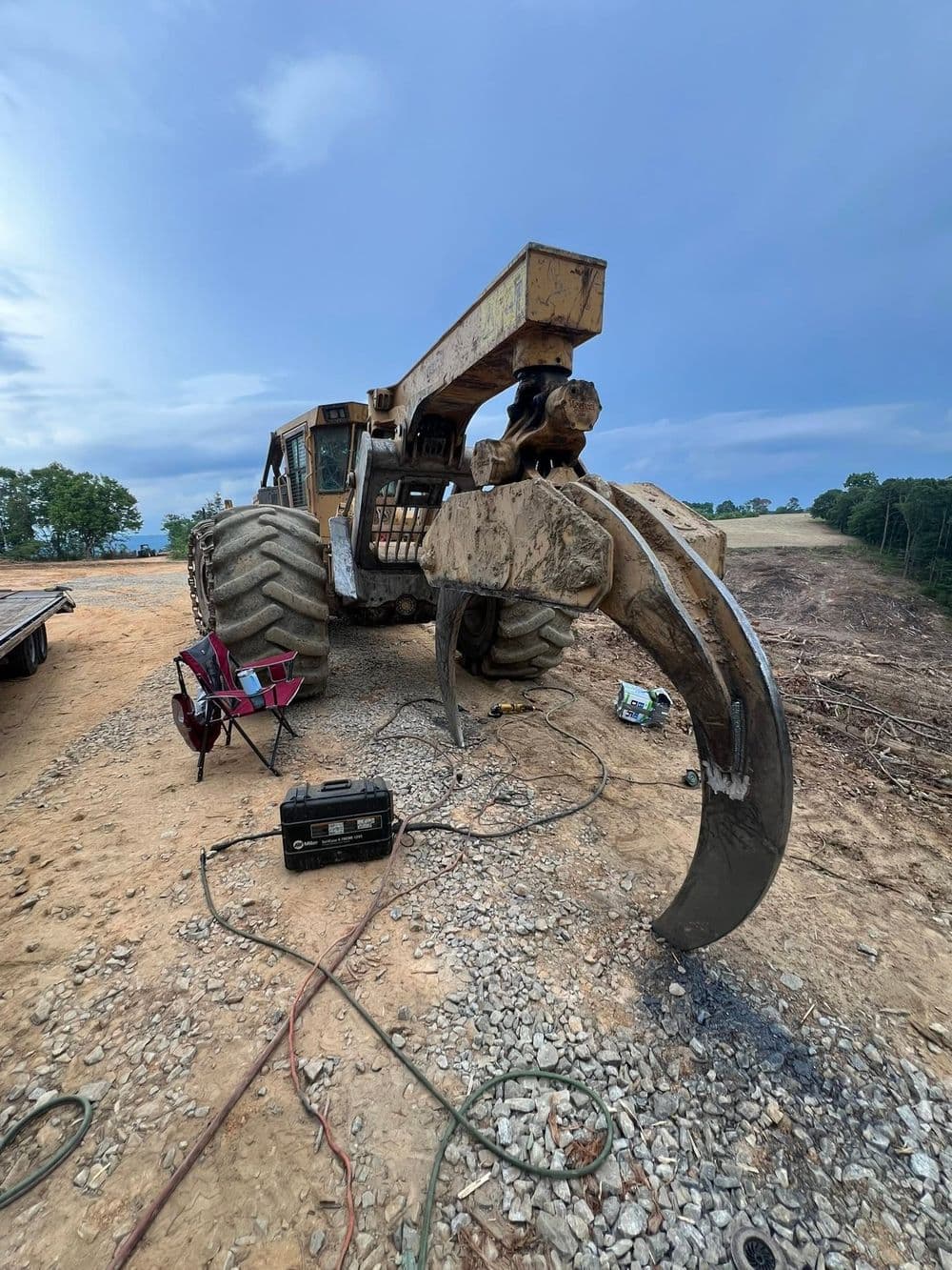 Heavy-duty tractor with claw attachment on construction site, surrounded by tools and debris.